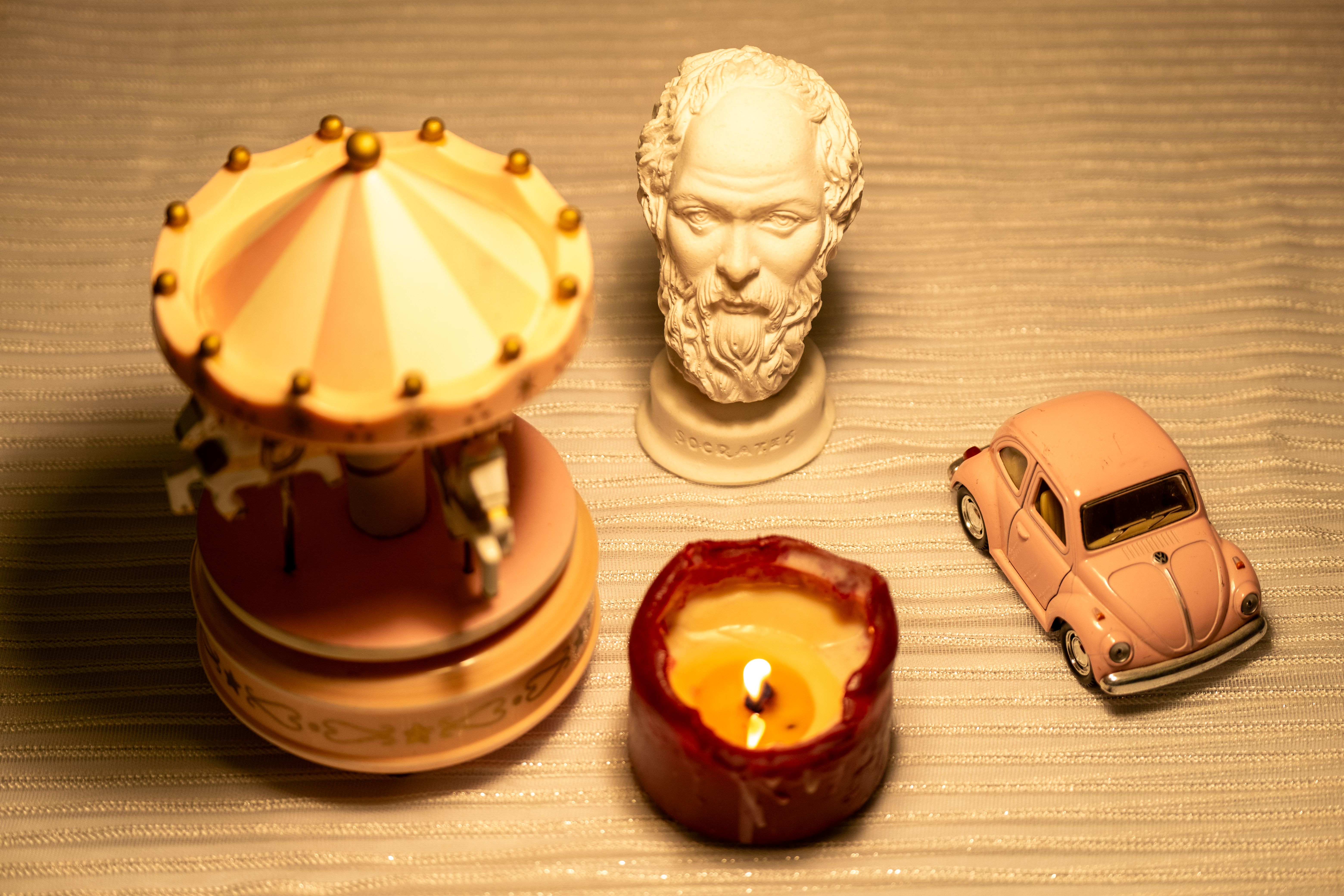 A serene still life featuring a bust, carousel, candle, and vintage car model.