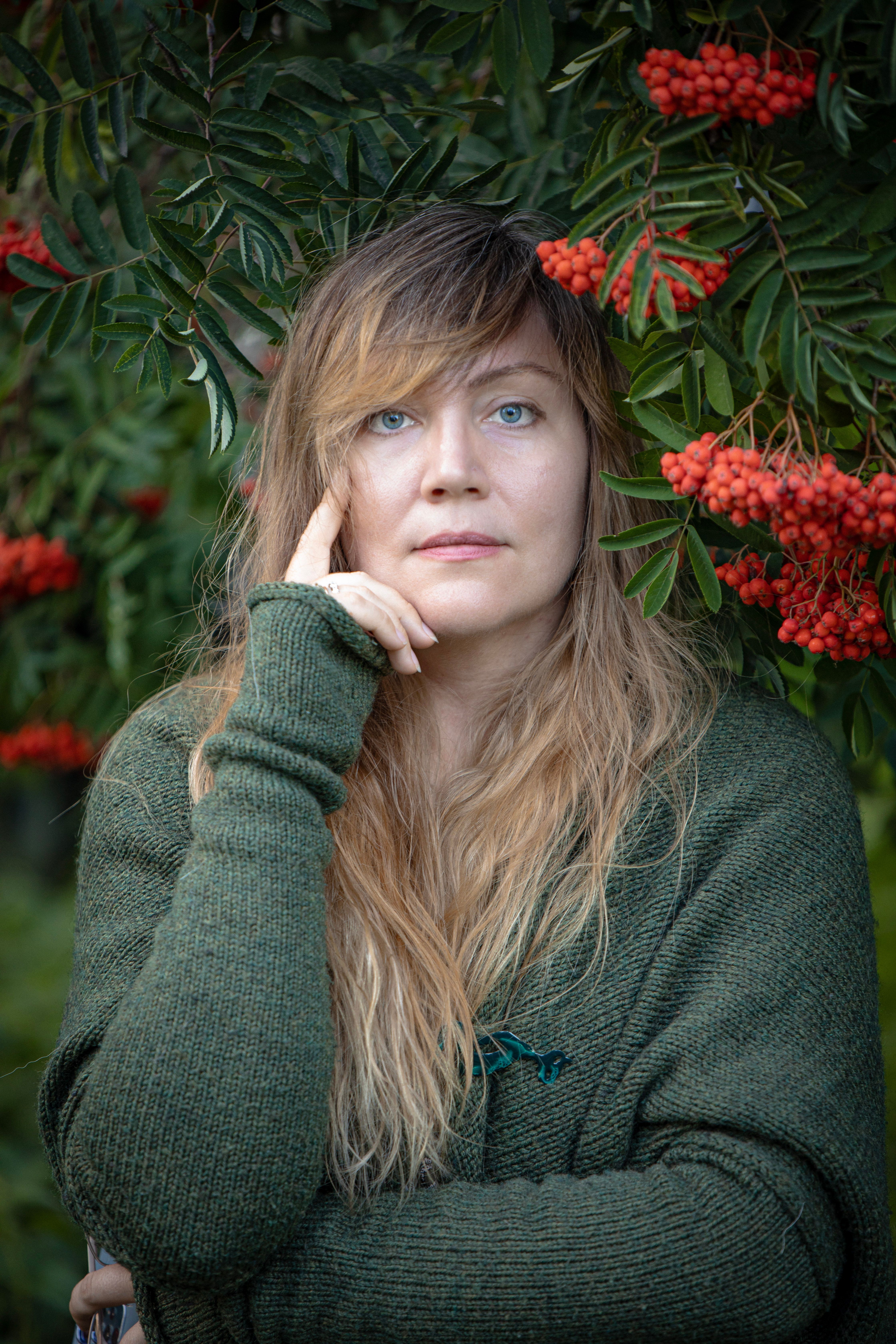 Portrait of a woman surrounded by green leaves and red berries, showcasing a serene autumn vibe.