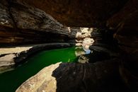 A tranquil limestone cave with a striking green water pool illuminated by sunlight.