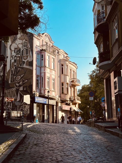Free A picturesque cobblestone street with historic architecture and street art in a European city, perfect for travel enthusiasts. Stock Photo