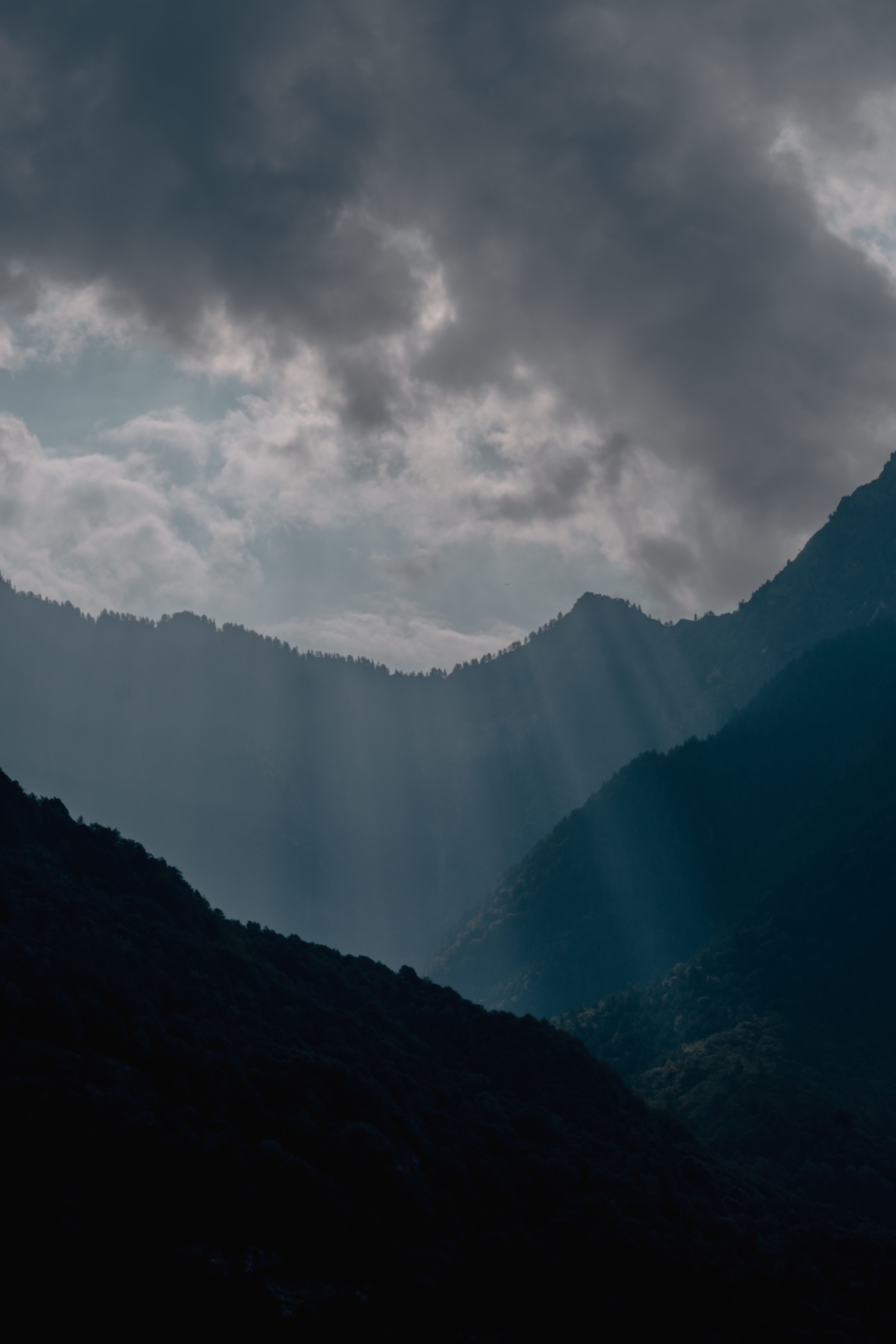 The sun shines through the clouds over a mountain range · Free Stock Photo