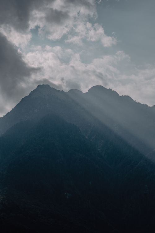 Free A serene mountain landscape with sun rays piercing through the clouds. Stock Photo