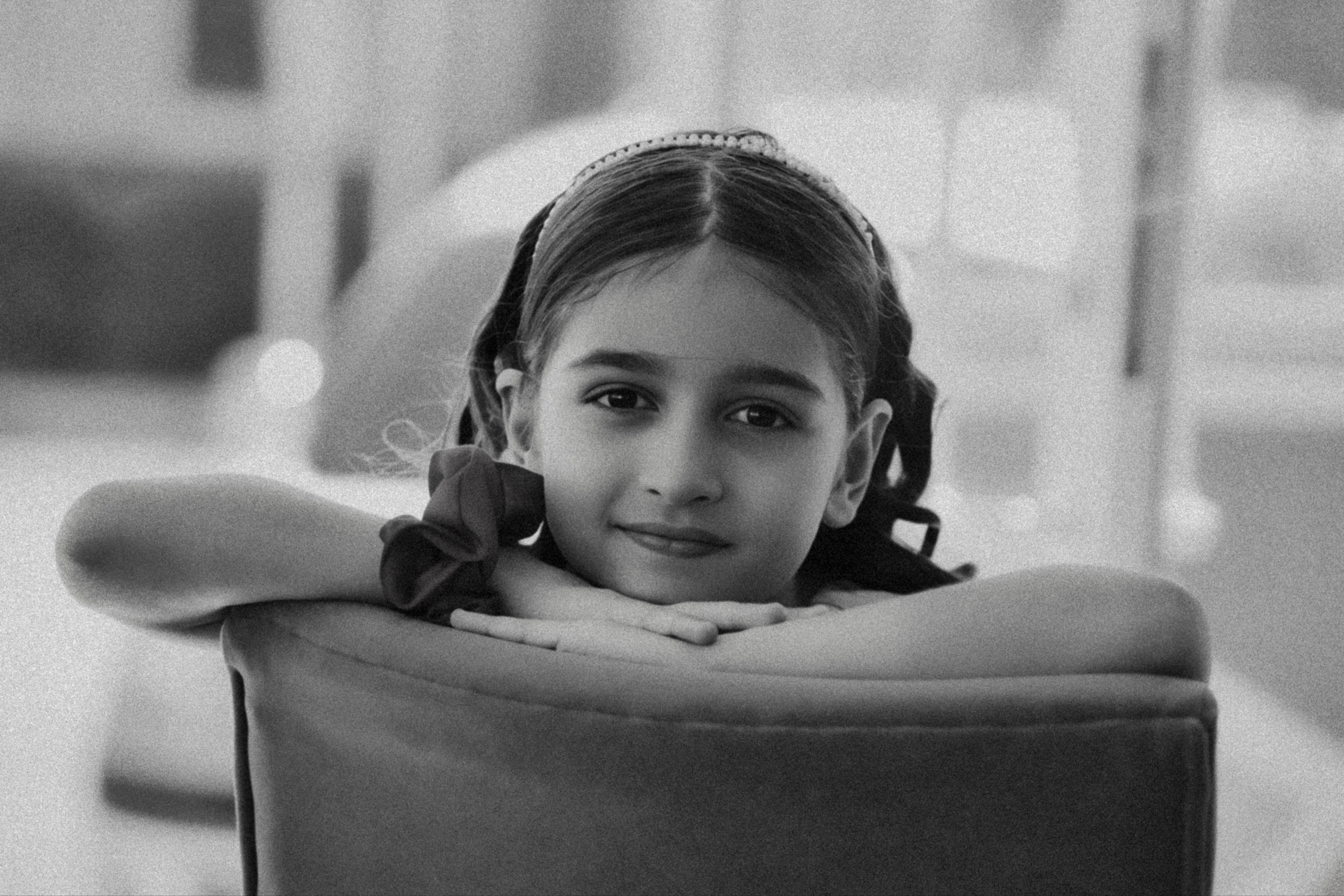 Charming black and white portrait of a young girl resting her head on a chair edge, indoors.