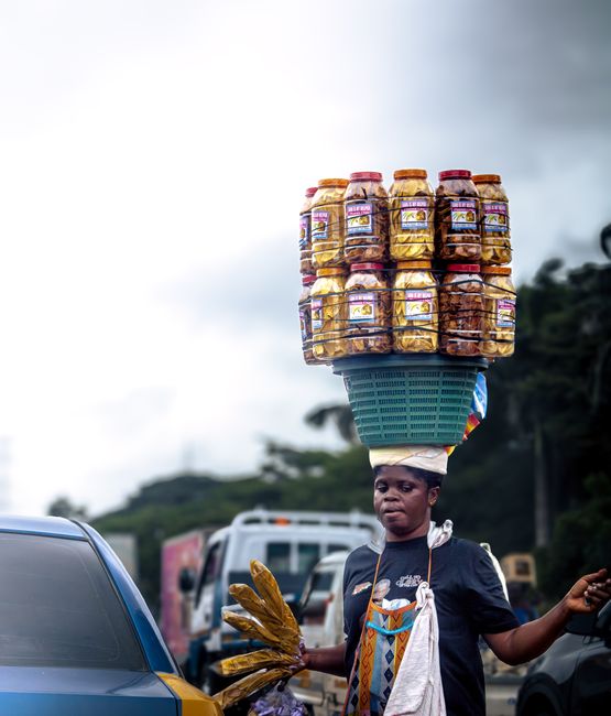 Woman balancing snack jars on her head while selling on the busy streets of Accra, Ghana.