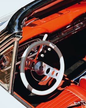 Close-up of a vintage convertible’s red dashboard and steering wheel, showcasing classic car design.