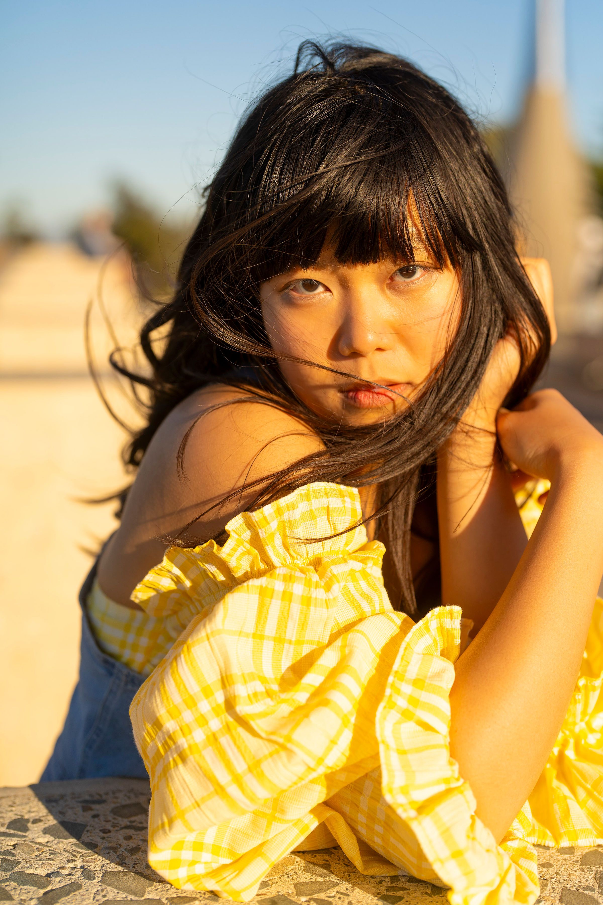 A woman enjoys a sunny day outdoors in a stylish yellow dress, embodying summer vibes.