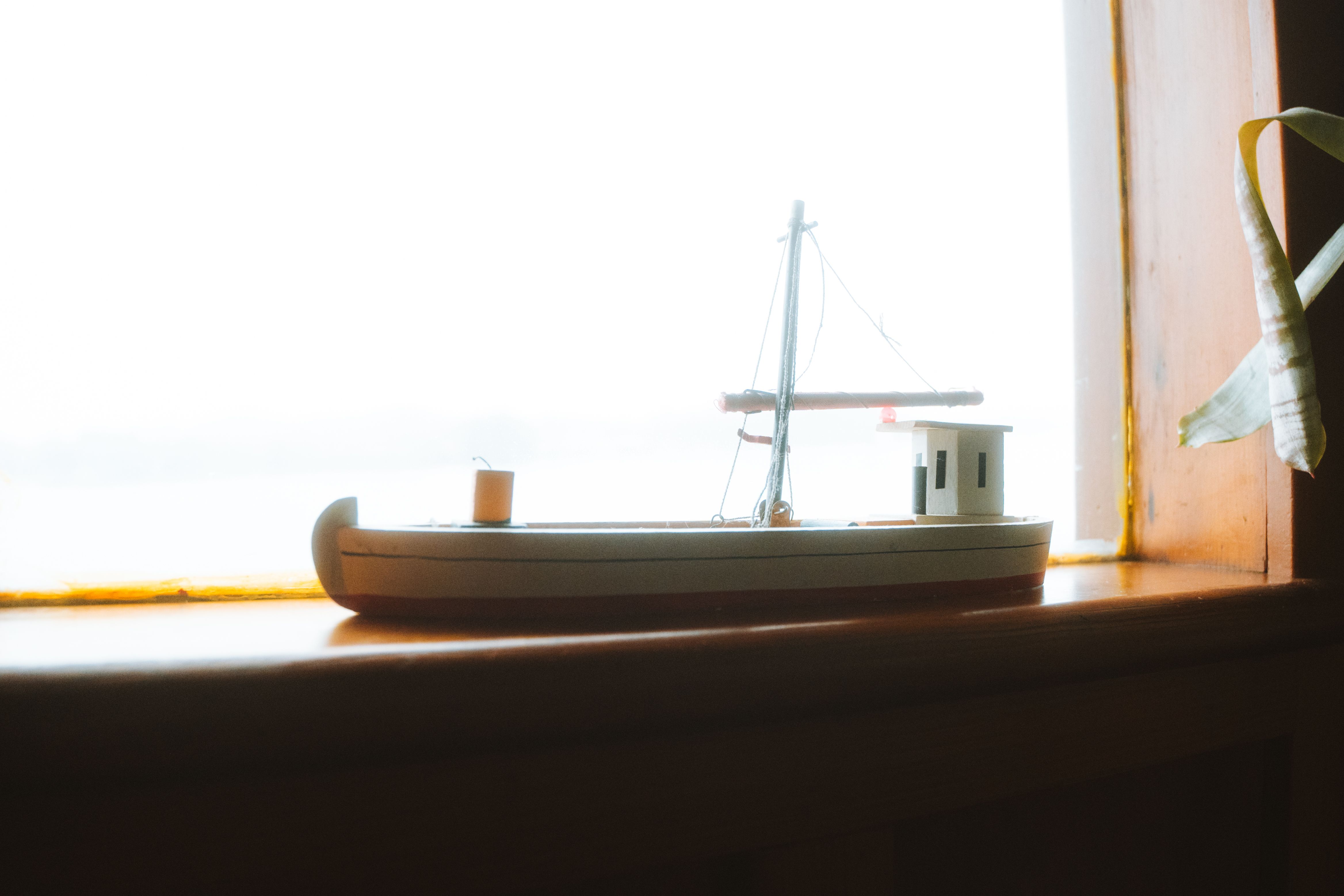 A miniature wooden sailboat displayed on a sunlit window sill, capturing a peaceful nautical vibe.