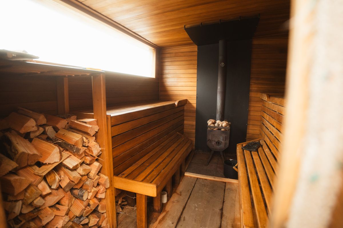Sauna finlandesa de madera con estufa de leña y leña apilada
