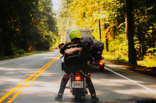 Free A motorcyclist waits on a scenic forest road, wearing a bright yellow helmet, showcasing adventure and travel. Stock Photo