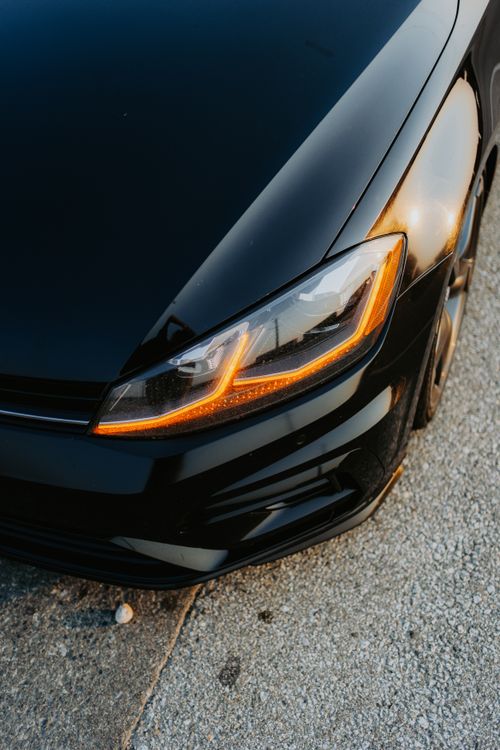Free Close-up of a sleek black car's headlight reflecting sunset light on asphalt. Stock Photo