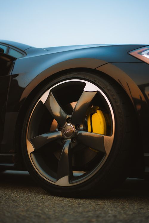 Free Dynamic close-up of a sleek sports car wheel with black rim and yellow brake caliper. Stock Photo