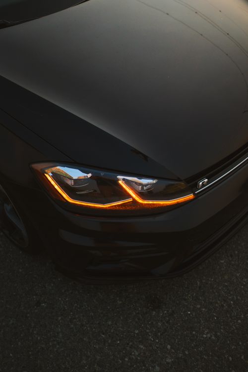 Free Close-up of a sleek black sports car with glowing headlights against a dark road. Stock Photo