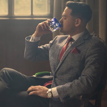 Elegant man in a suit sipping a drink in a cozy indoor setting, embodying sophistication.