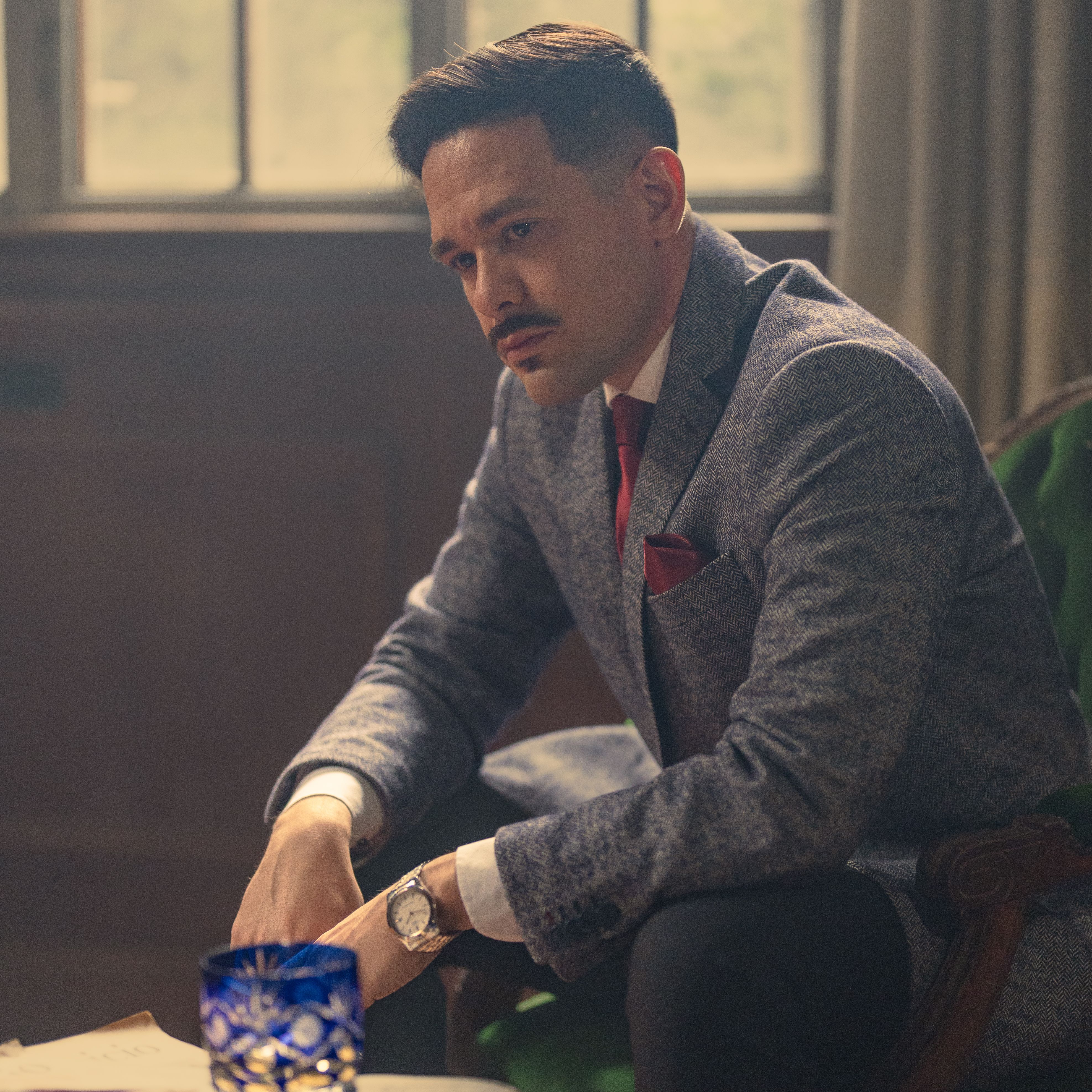 A well-dressed man in a vintage suit sits in a dimly lit room, evoking classic elegance.