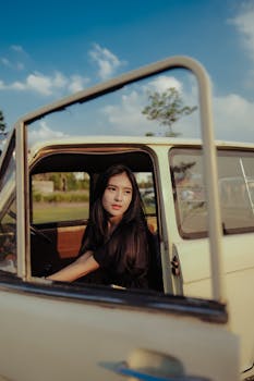 A woman sits inside a vintage car, enjoying a beautiful sunny day with a clear blue sky.