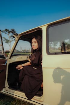 A young woman in a vintage car enjoying a sunny day outdoors.