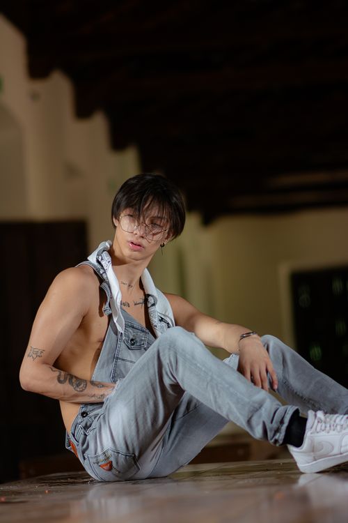 Free Artistic portrait of a young man in denim overalls lounging indoors with a moody vibe. Stock Photo