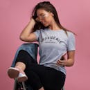 一位时尚女性身着休闲装，戴着眼镜，在粉色背景前摆姿势