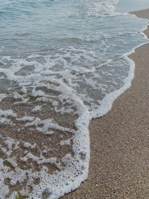 Free Tranquil seashore with ocean waves gently lapping onto sandy beach, perfect for travel and relaxation themes. Stock Photo