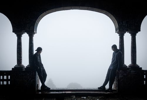 Free Silhouettes of two people leaning against an archway in foggy surroundings, creating a moody ambiance. Stock Photo
