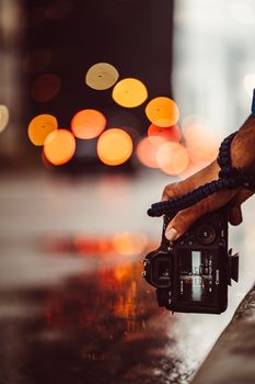 Photographer holding a camera, capturing reflections of city lights on a wet surface.