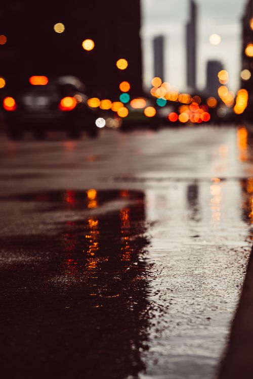 Free Blurred cityscape with wet street reflections and bokeh lights at dusk, creating a moody urban atmosphere. Stock Photo