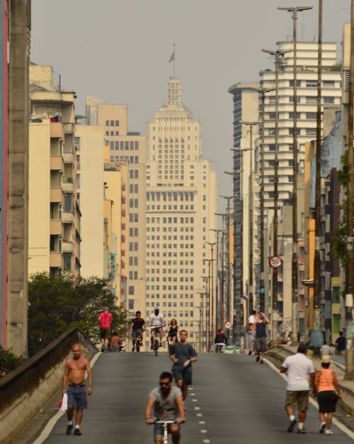 Free A bustling street in Sao Paulo, Brazil, featuring people walking and cycling amidst tall skyscrapers. Stock Photo