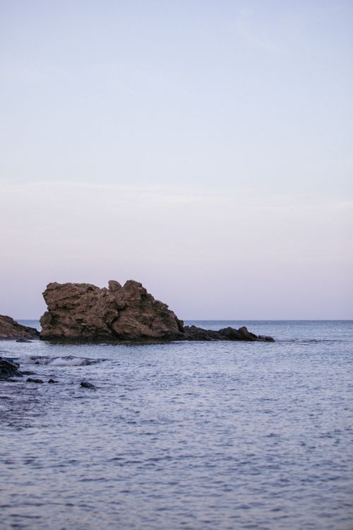 Free Peaceful ocean scene with a rocky outcrop at dusk, captured during summer. Stock Photo