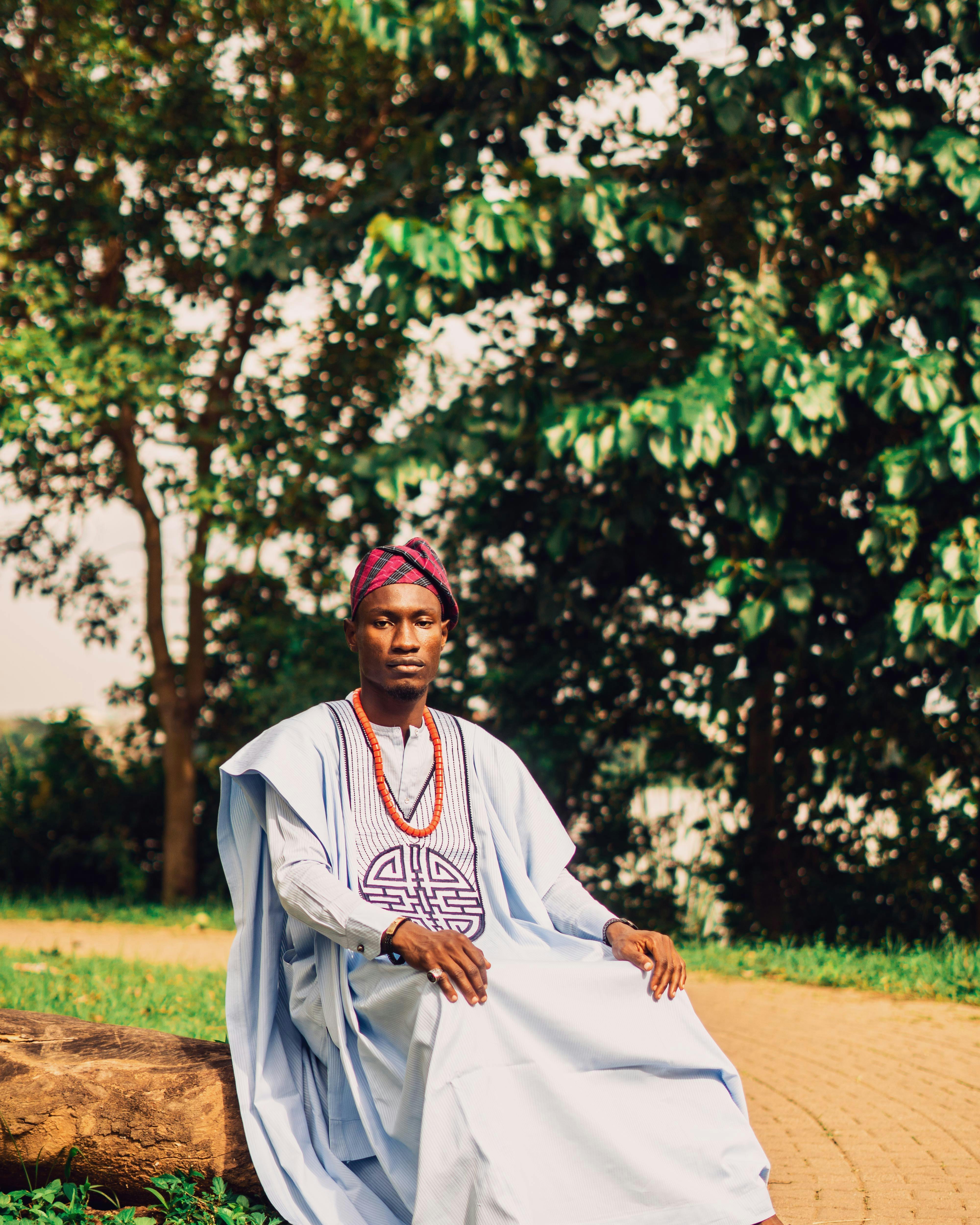 A man in traditional African attire enjoys a serene moment in a lush green park.