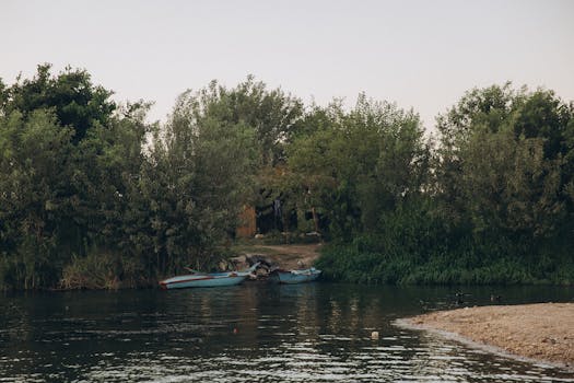Tranquil river scene at Al Qanatir, Egypt with lush greenery and small boats.
