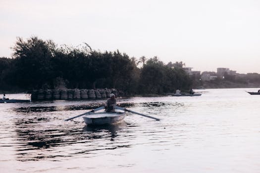 A serene scene of a person rowing a boat on the Nile River during sunset in Al Qanatir Al Khayriyyah, Egypt.