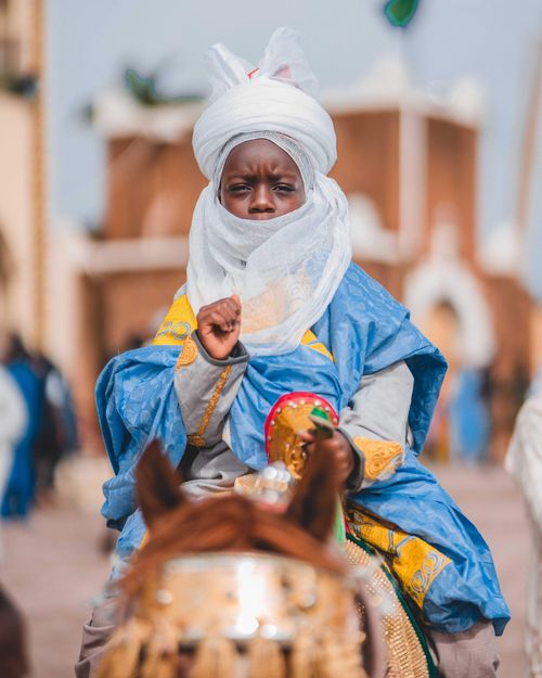 Free A child in vibrant traditional clothing and turban rides a horse during a festival in Zaria, Nigeria. Stock Photo