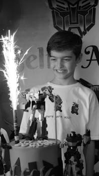 Joyful child celebrating a birthday with toy robots and cake fireworks indoors.