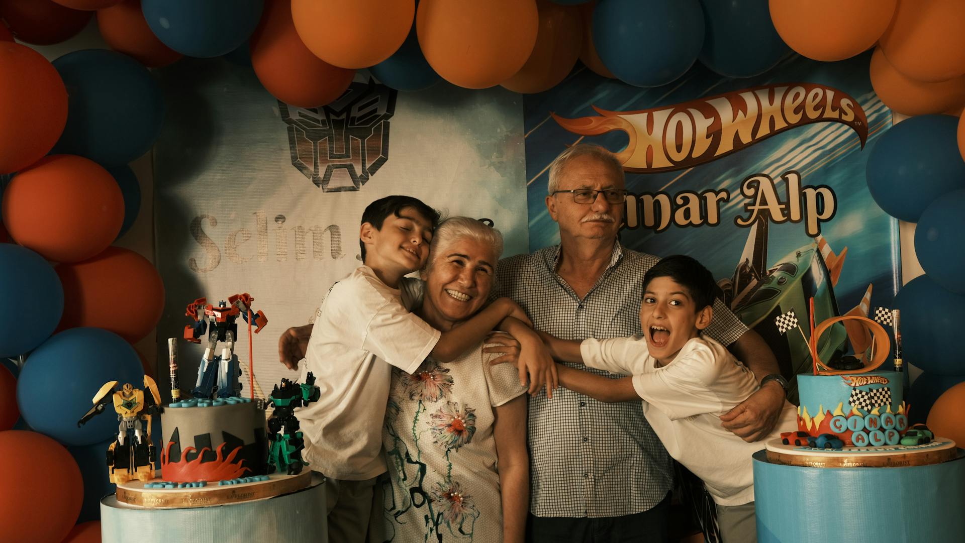 A family poses for a photo in front of a hot wheels cake