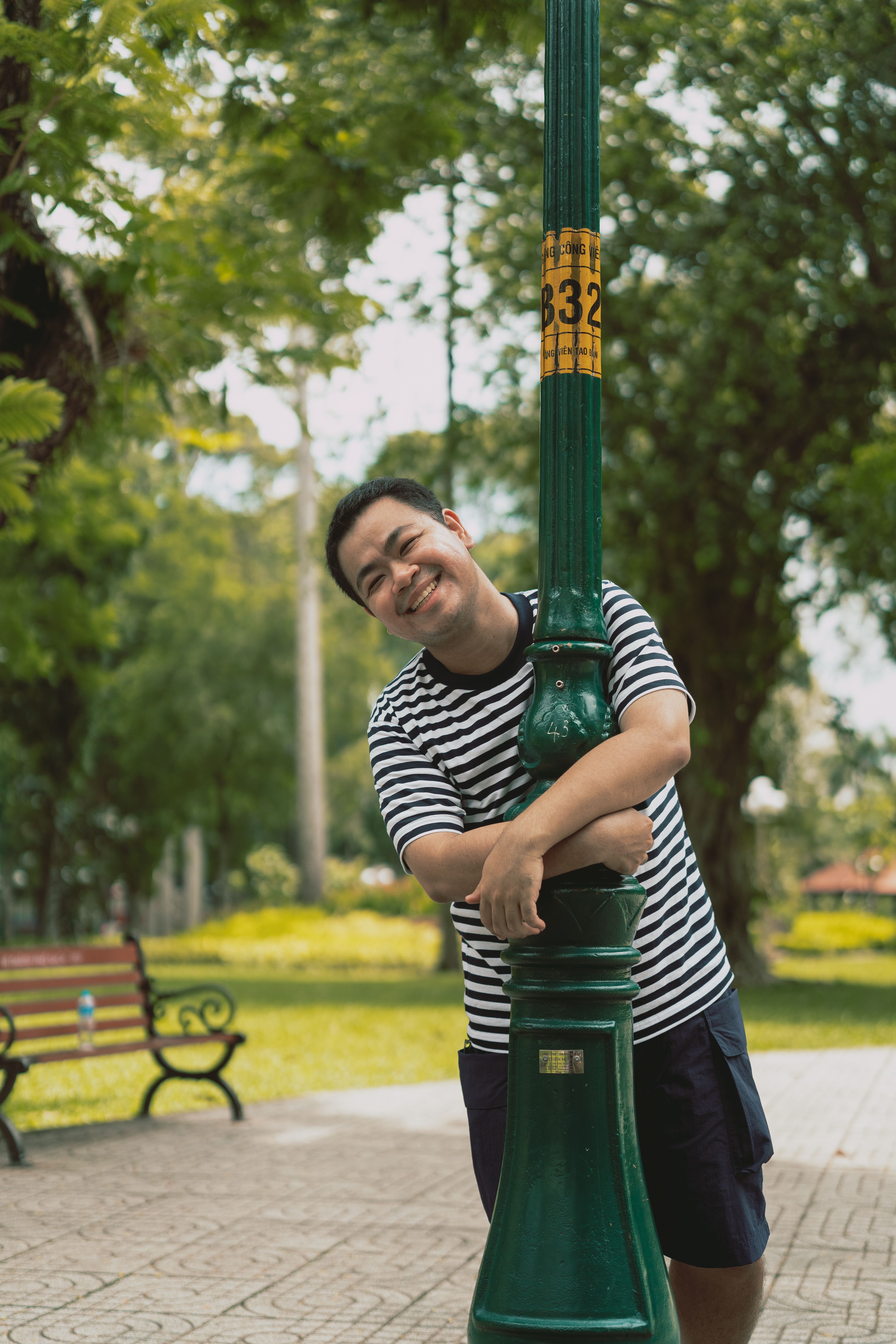 A person in stripes happily embraces a lamp post in a vibrant park.