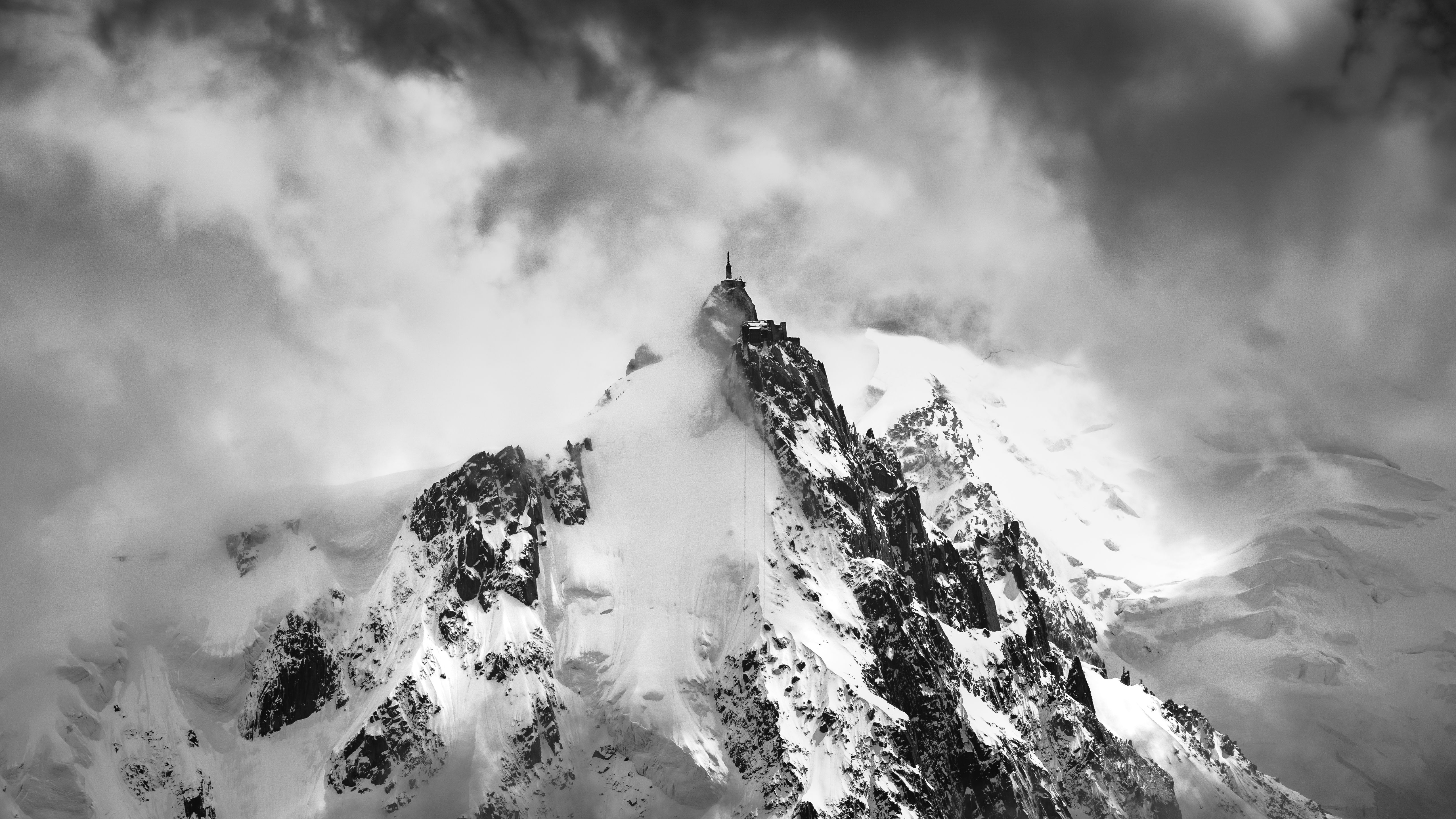 A dramatic black and white photograph of Aiguille du Midi shrouded in clouds, showcasing its majestic peak.
