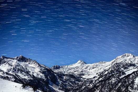 A breathtaking night sky with star trails above snow-covered mountains, creating a majestic winter landscape.