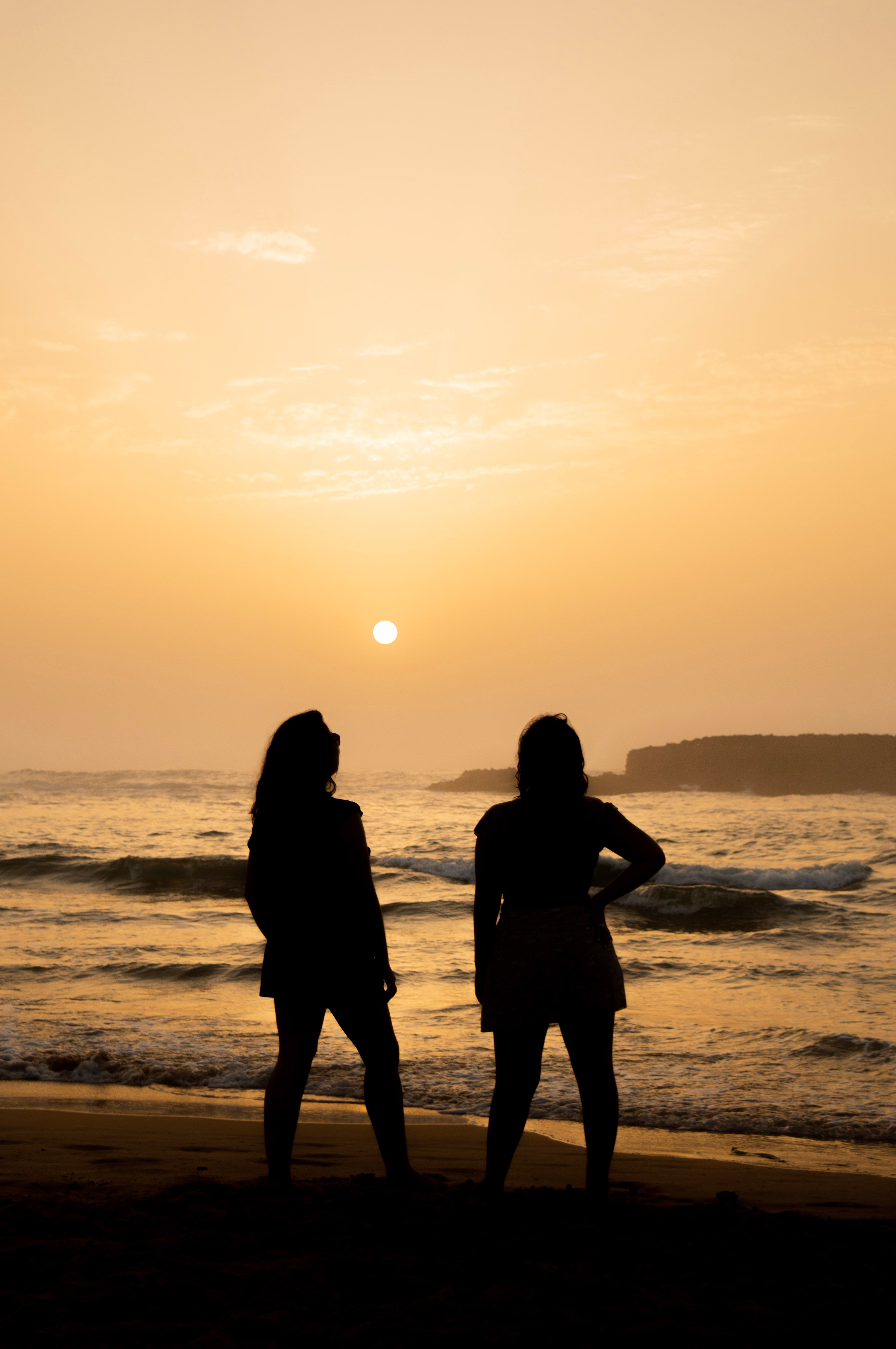 Two women standing on the beach at sunset · Free Stock Photo