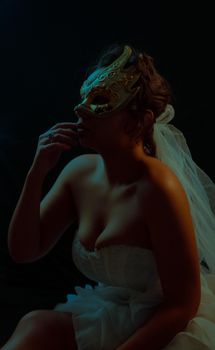 Elegant woman in a bridal dress and ornate mask in atmospheric lighting, evokes mystery.