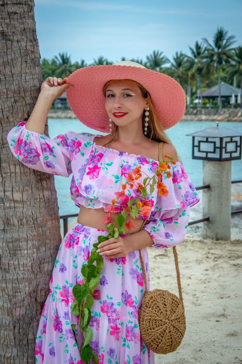 Free Woman in a floral dress and straw hat posing by a palm tree on a tropical beach Stock Photo