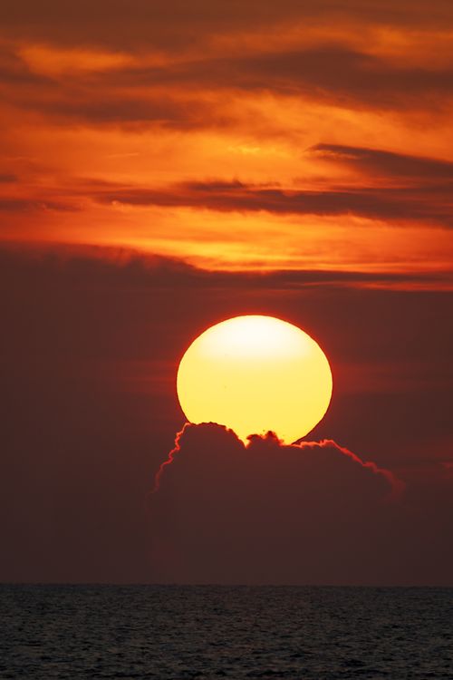Free Captivating sunset over ocean waters with a vibrant, glowing sun descending on the horizon. Stock Photo