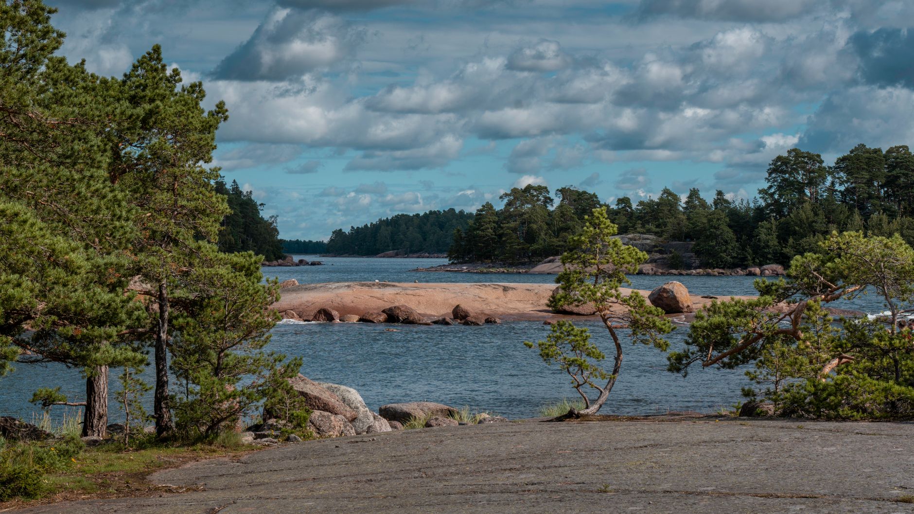 Tranquil seascape with pine trees and rocky islands under a cloudy sky.