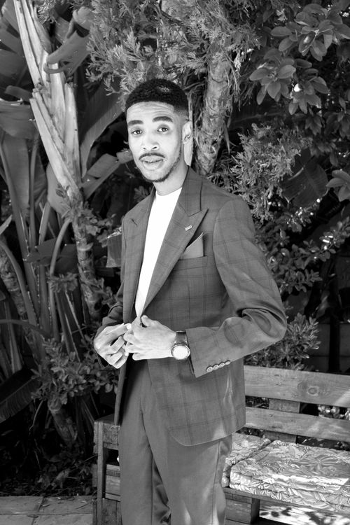 Free Black and white portrait of a man in a suit standing outdoors among greenery. Stock Photo