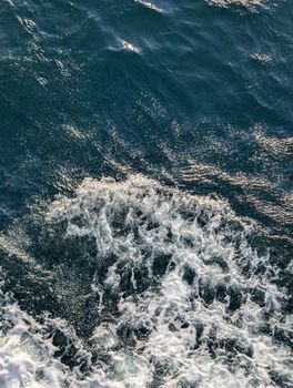 Dynamic aerial shot capturing ocean waves crashing and creating foam on the water surface.