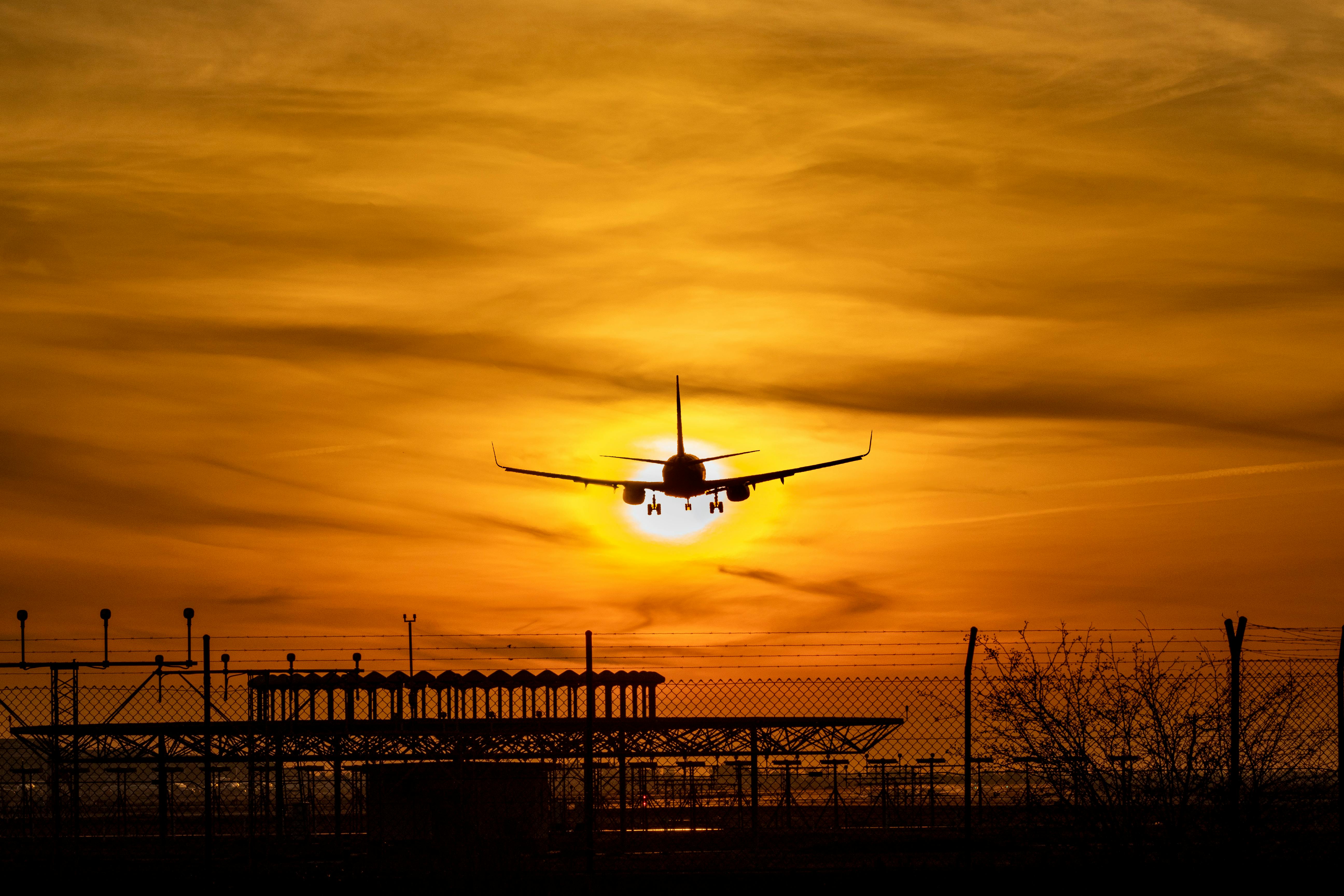 Free Silhouette of an airplane landing as the sun sets at El Prat Airport, highlighting vibrant orange skies. Stock Photo