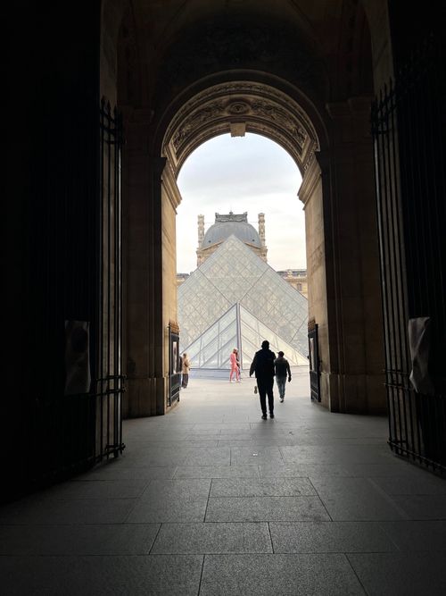 Free Silhouetted figures at the iconic Louvre Pyramid entrance in Paris, France. Stock Photo