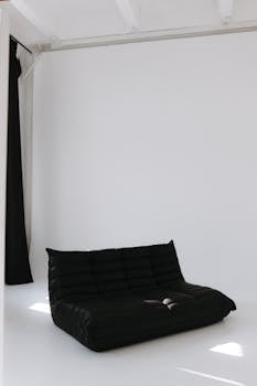 Black modern sofa in a minimalist white room with natural light.