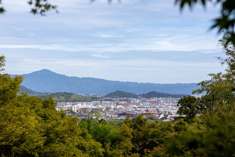晴れた空の下で、緑豊かな京都の景色と山々の背景が広がる美しい風景。