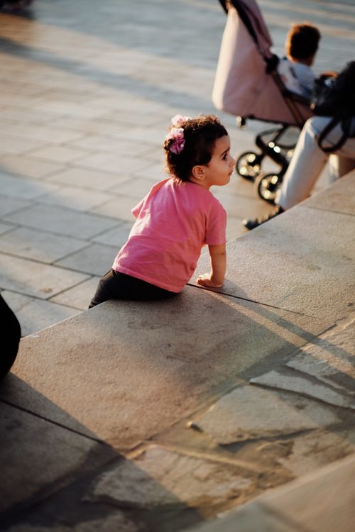 Free A young girl in a pink shirt exploring and climbing a city step, embodying innocence and curiosity. Stock Photo