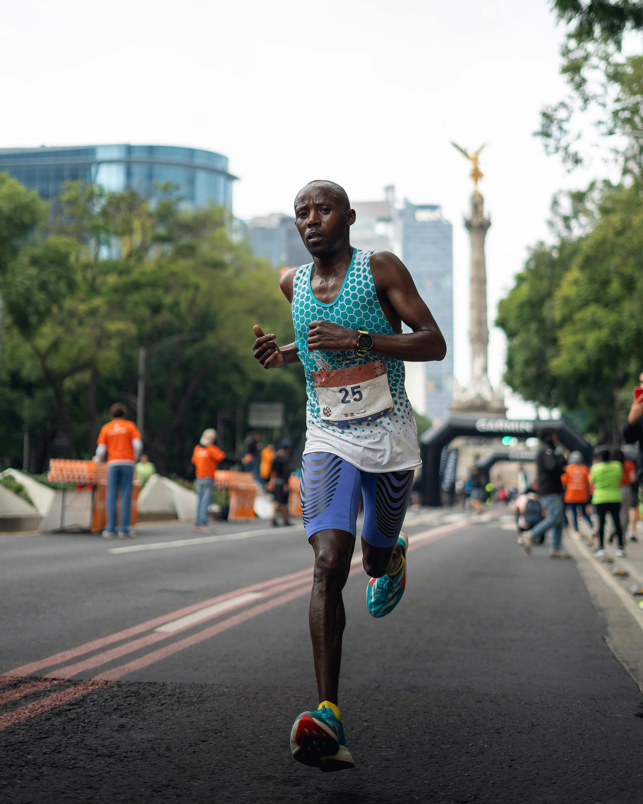 Focused runner participating in an urban marathon near a city landmark with support staff in the background.